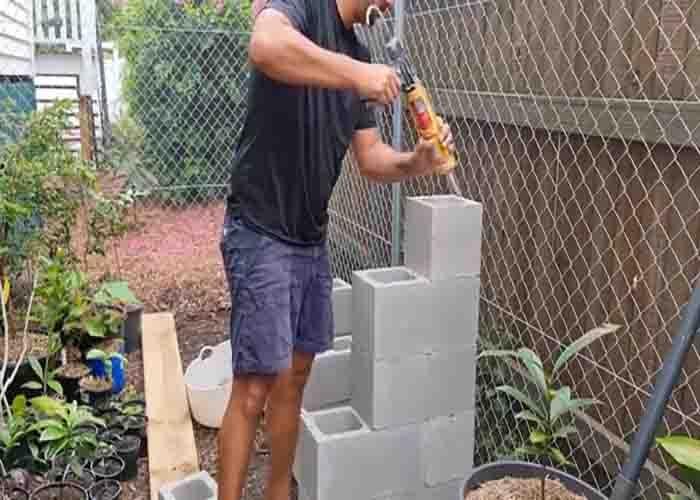 Building the DIY cinder block plant shelf with staggered blocks glued together and timber sleepers laid on top