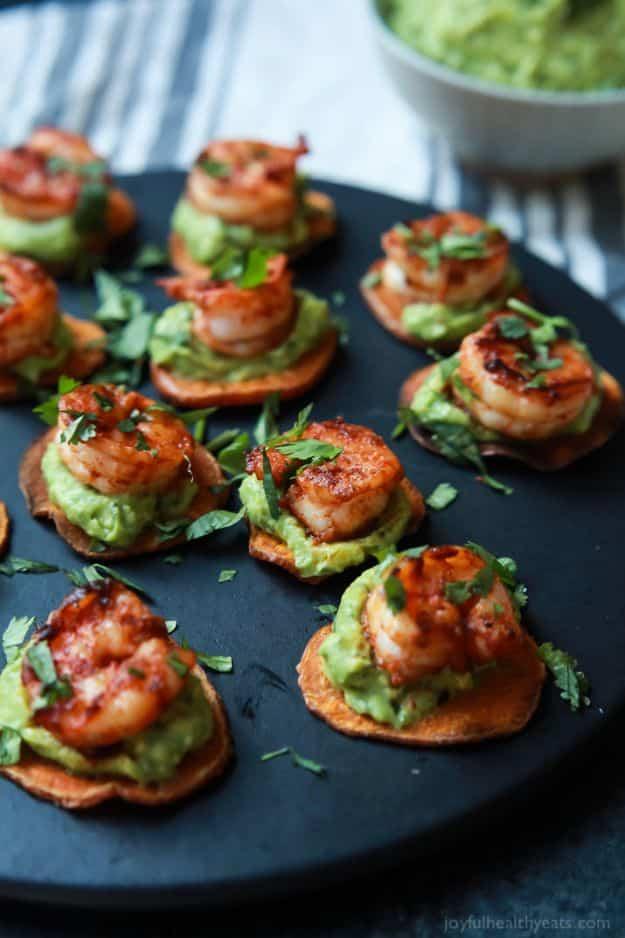 Roasted sweet potato rounds topped with green guacamole and Cajun shrimp with cilantro on a dark plate