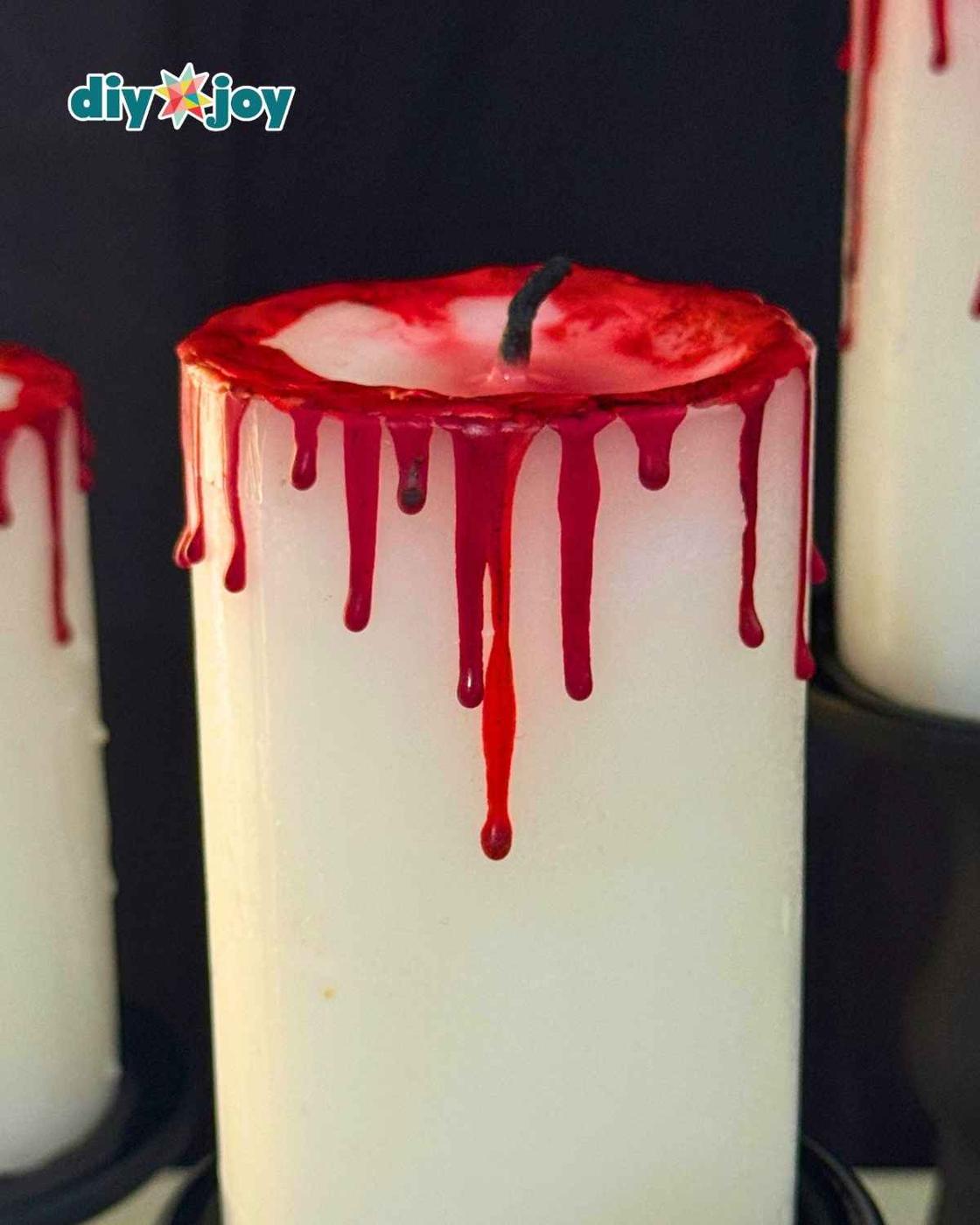 Finished DIY bloody candle glowing as spooky Halloween party decor with red wax drips made from melted crayons.