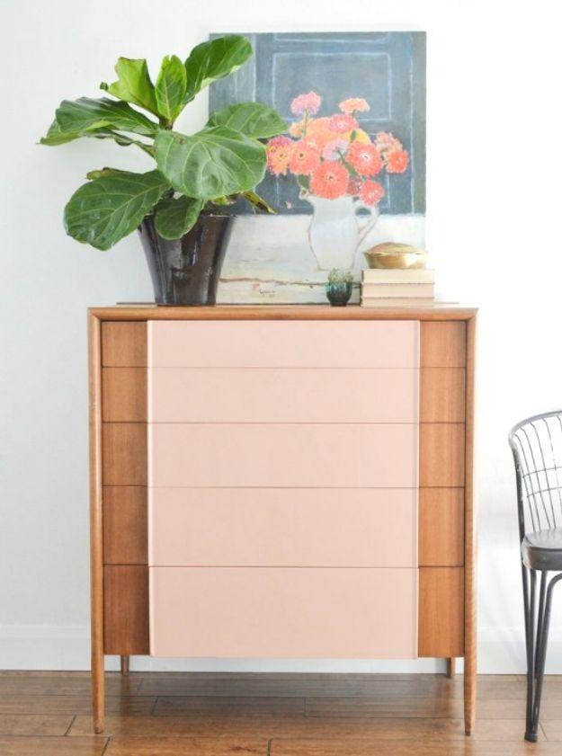 Wood dresser with five drawer fronts painted flat pale pink, tapered legs, a fiddle leaf fig and a floral still life above