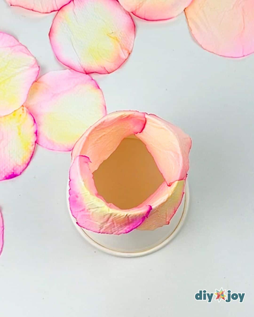 Paper flower making step, hands gathering and crumpling colored tissue petals into a soft rose shape