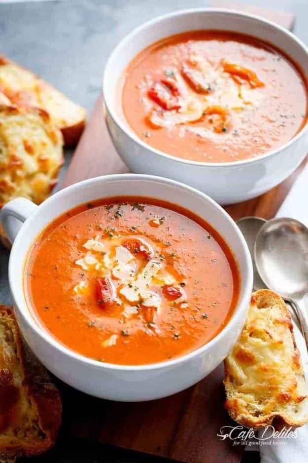 Creamy roasted tomato basil soup in two white bowls with grated cheese on top and cheesy bread beside
