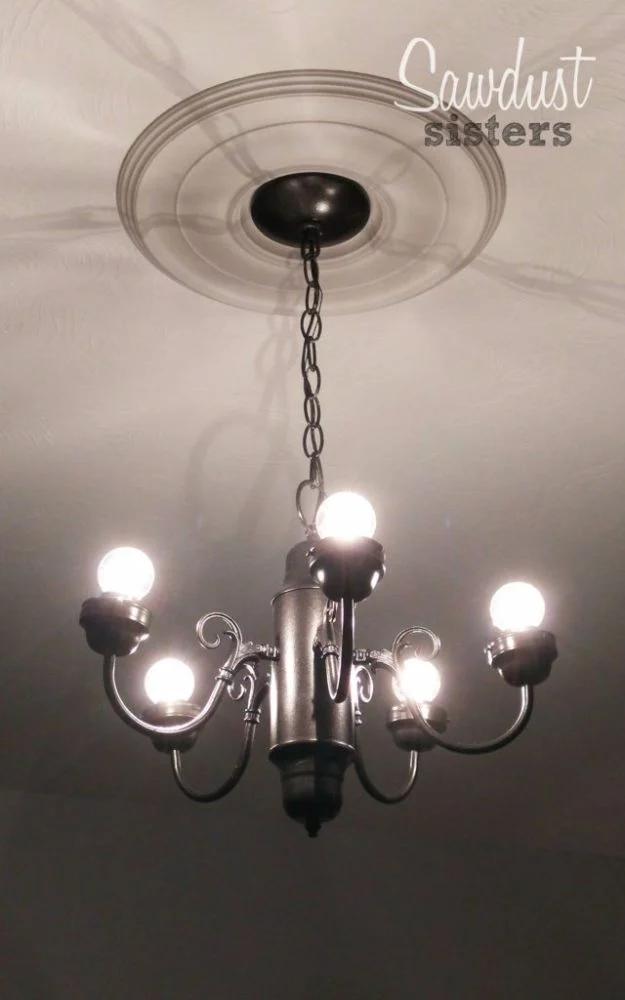 Simple silver chandelier makeover lit from below, hanging on a short chain from a wide round plaster ceiling medallion