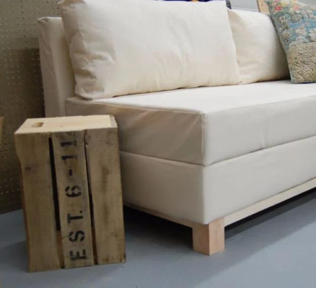 Boxy cream upholstered storage sofa on square wooden feet beside a stencilled pallet crate in a garage