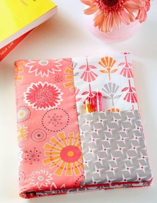 Handmade journal cover sewn in coral and orange floral fabric over a spiral notebook with a pieced pocket panel