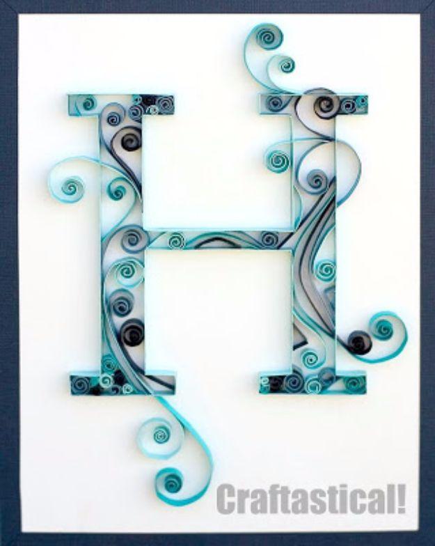 Quilled paper monogram letter H in blue and black scrolls on white, mounted inside a dark navy picture frame