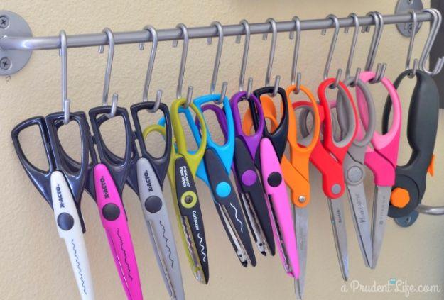 Wall rail with S hooks holding thirteen pairs of scissors and decorative paper edgers in pink, orange, green and black