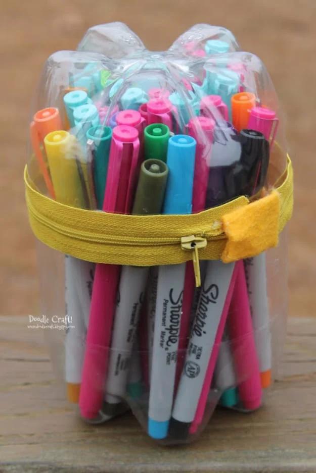 Clear soda bottle pencil case made from two bottle bottoms joined with a yellow zipper, filled with colorful markers