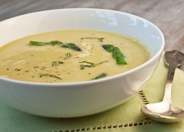 Asparagus soup in a white bowl, smooth pale cream puree topped with green asparagus tips and a spoon