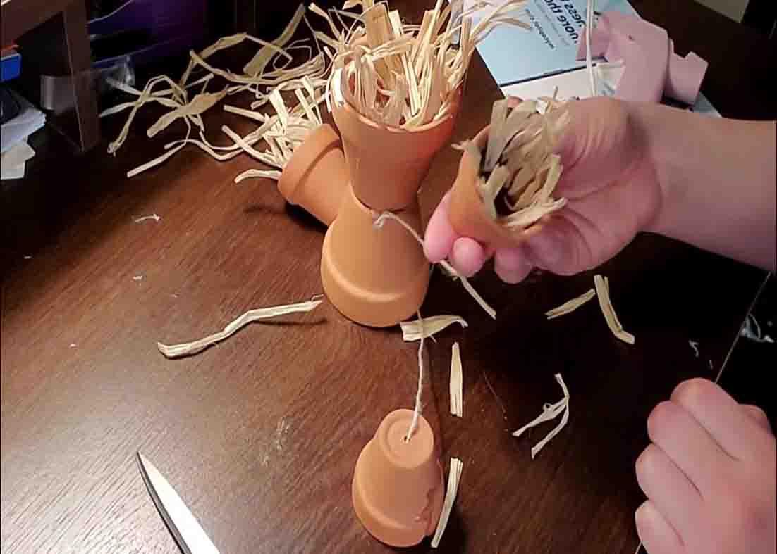 Adding raffia to the terracotta pot scarecrow to decorate it