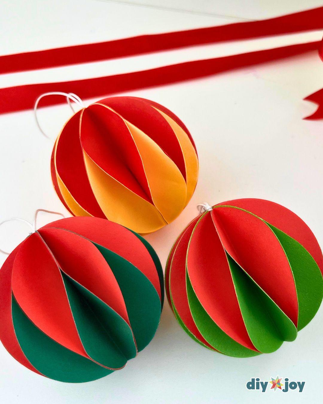 Budget Friendly Crafts - three finished paper ball ornaments in red, yellow, and green resting on a white surface under a draped red ribbon