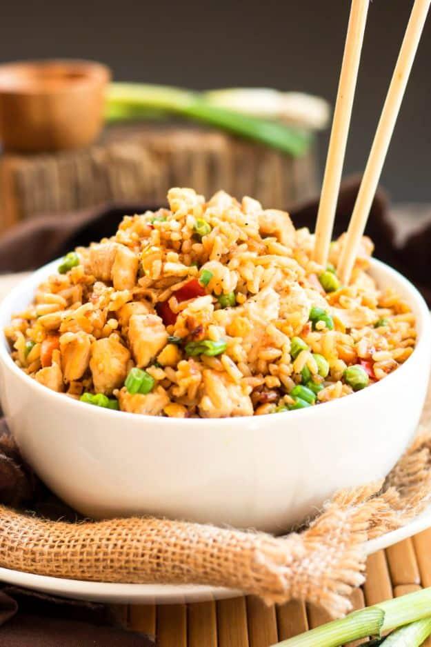 Gluten free chicken fried rice with peas, diced carrot and green onion in a white bowl with chopsticks standing upright