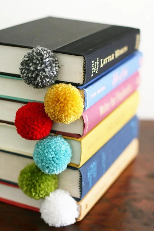 Yarn ball and string bookmarks tucked inside a stack of colorful books, a cute handmade craft to sell