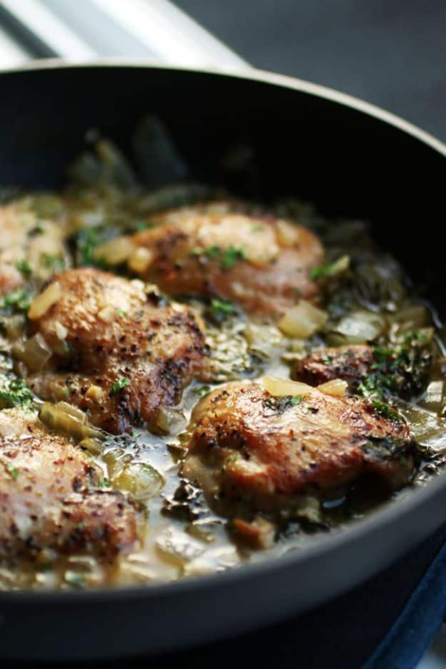 Easy lemon garlic chicken, browned chicken thighs in a dark skillet with onion and wilted spinach in pan sauce