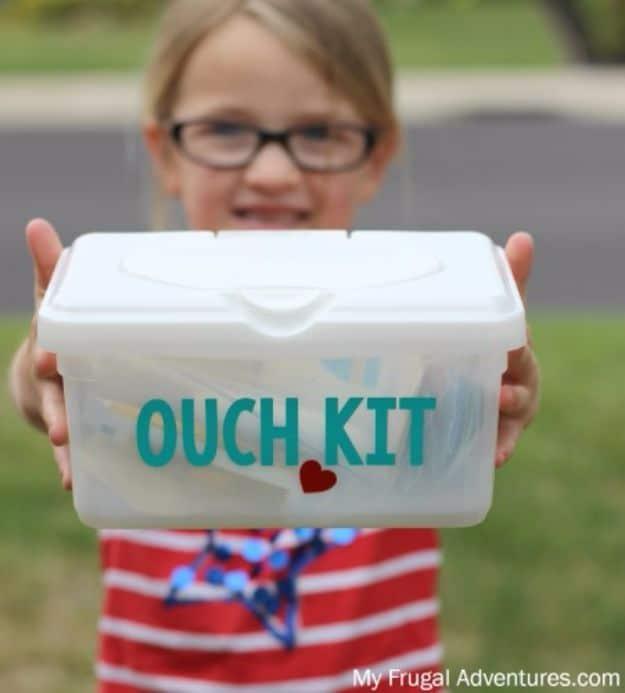 DIY car first aid kit in a white wipes tub labeled Ouch Kit in teal letters, held out by a young girl