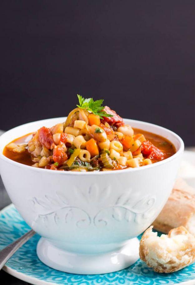 Minestrone soup in a fluted white bowl with beans, tomato, small pasta and parsley, bread roll beside