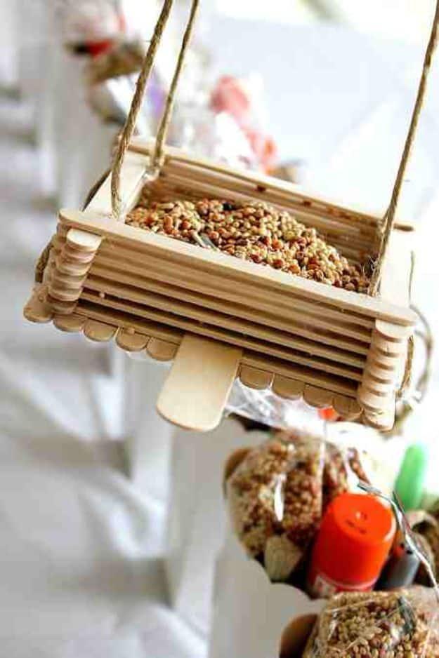Popsicle stick bird feeder filled with seed, hanging from twine at a party table with craft kit bags behind it