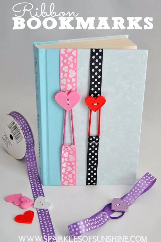 Three ribbon bookmarks in pink hearts, black polka dot and purple wrapped around a blue hardback book with buttons