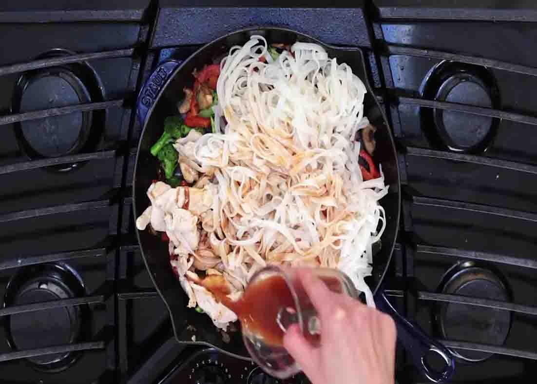 Pouring the sauce over the chicken stir dry with rice noodles
