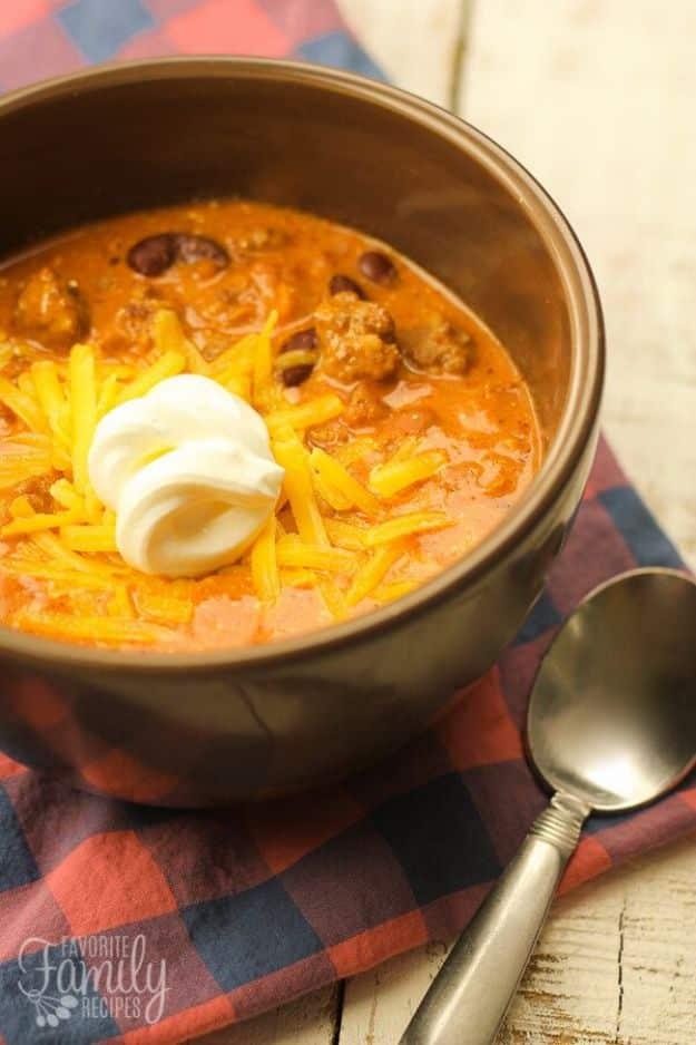 Creamy Italian sausage chili in a dark bronze bowl with shredded cheddar and sour cream on a red plaid cloth