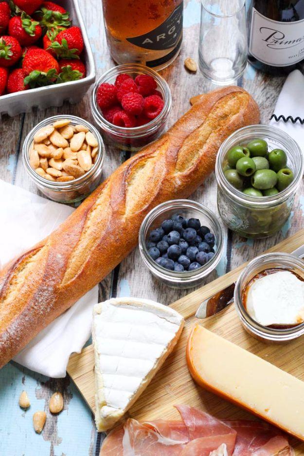 Pack a picnic for wine tasting, a baguette with brie, berries, olives, cashews and wine bottles arranged on a blue table