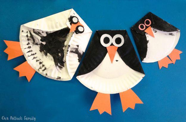 Three paper plate penguins with folded black painted wings, orange beaks and feet, on a bright blue background