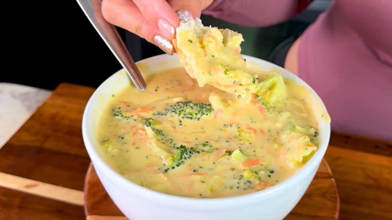 Copycat Panera broccoli cheddar soup in a white bowl with broccoli and carrot, bread being dipped in