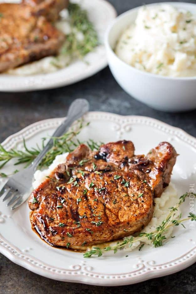 Maple balsamic glazed pork chop seared golden brown with fresh thyme, served over mashed potatoes on a white plate