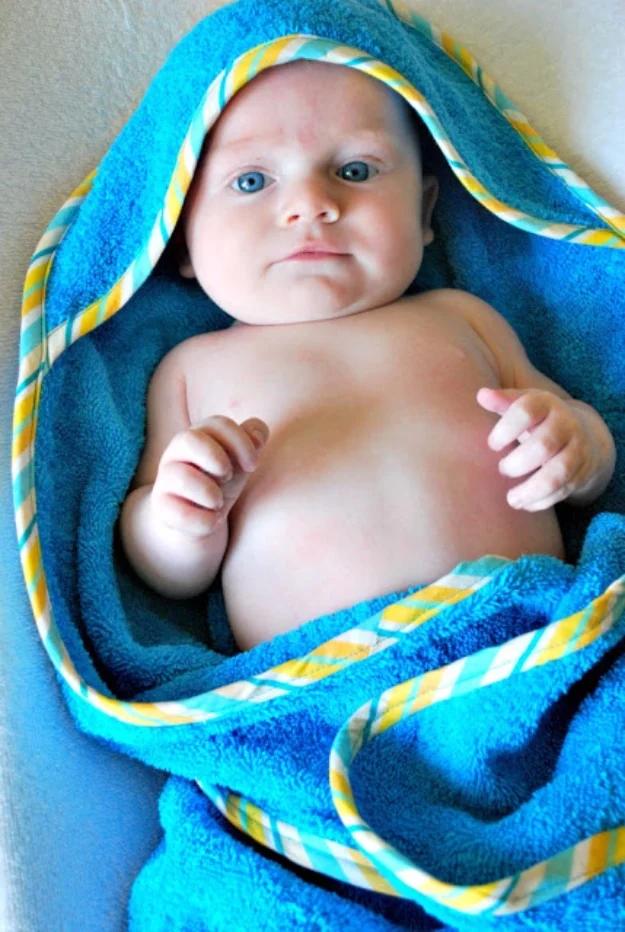 Newborn baby wrapped in a teal hooded towel with yellow and blue striped binding round the hood edge