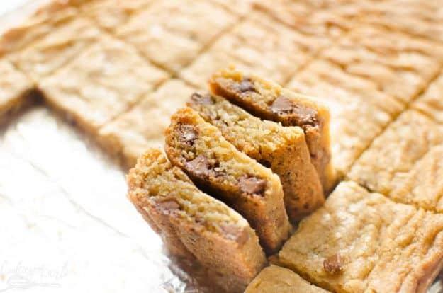 A whole pan of blonde brownies scored into squares with three standing on edge to show the chocolate chips