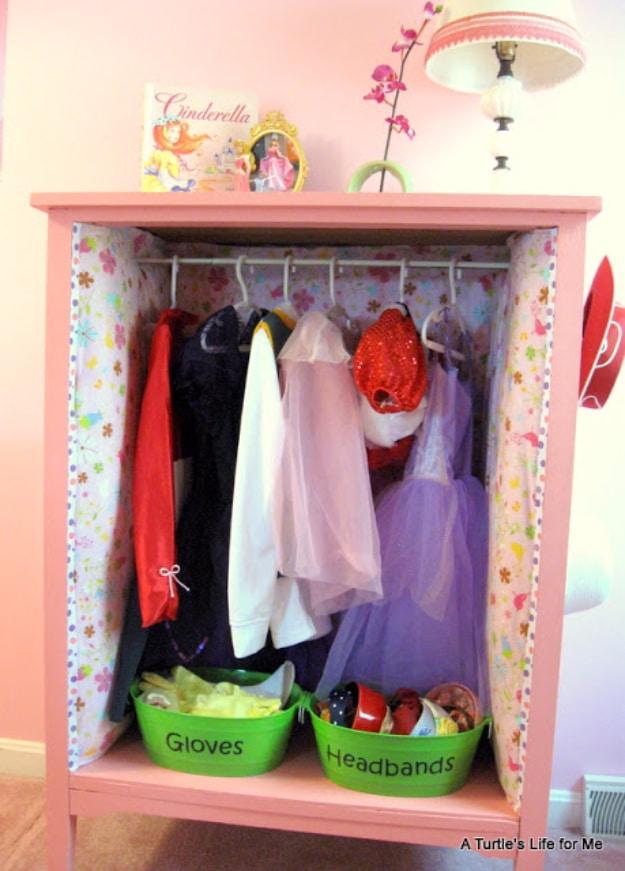 Dress up headquarters, a pink painted dresser shell lined with floral fabric holding costume dresses and labeled green bins