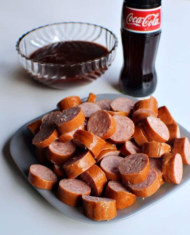 Coca Cola slow cooker BBQ kielbasa, sliced sausage rounds on a grey plate beside a dish of dark sauce and a Coke bottle