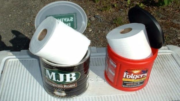 Two plastic coffee canisters, one MJB and one Folgers, each holding a roll of white toilet paper inside