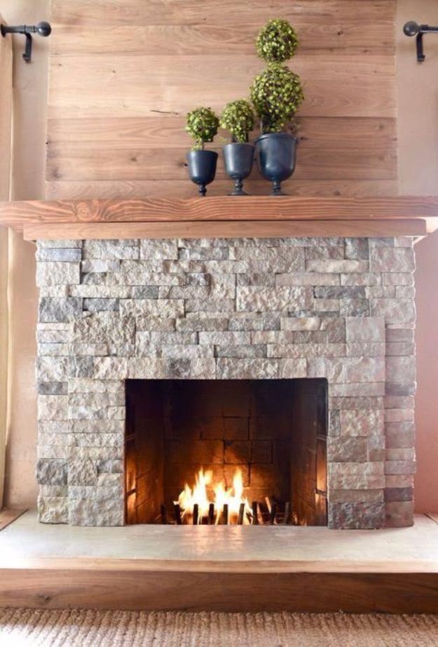 Stone veneer fireplace with a lit fire, a thick reclaimed wood mantel, plank wall above and three topiaries in black urns