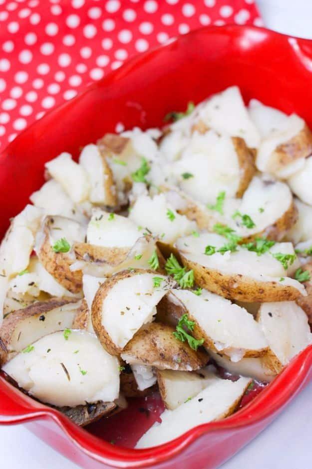 Red baking dish filled with sliced herbed potatoes flecked with parsley on a red and white polka dot cloth