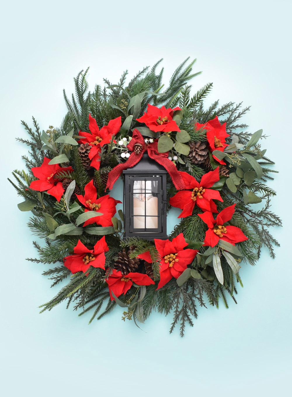 Full green wreath with red berries and a black lantern wired into the center hanging on a front door