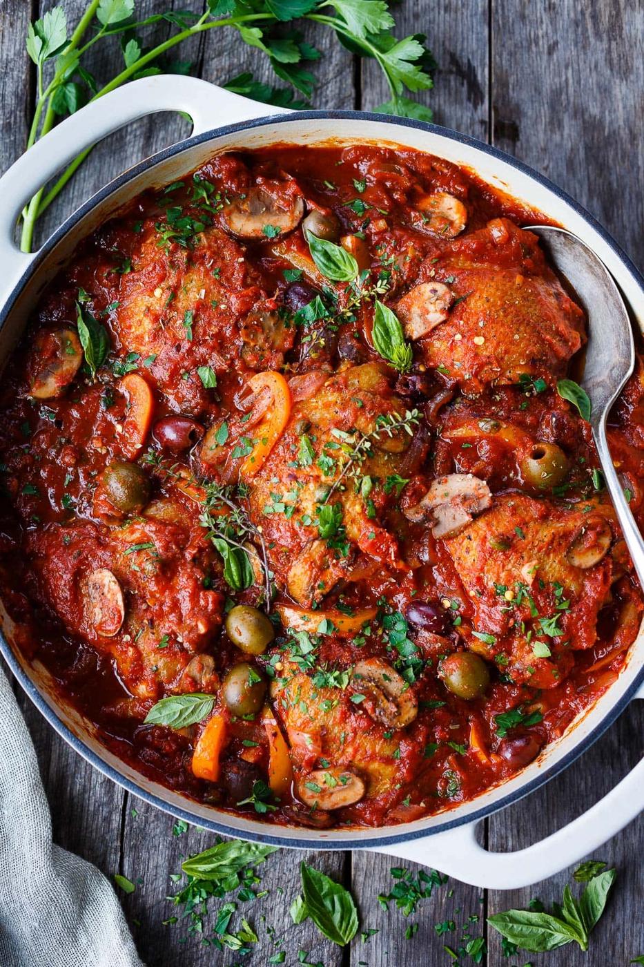 Traditional chicken cacciatore in a white pan, chicken in red sauce with green olives, mushrooms and basil