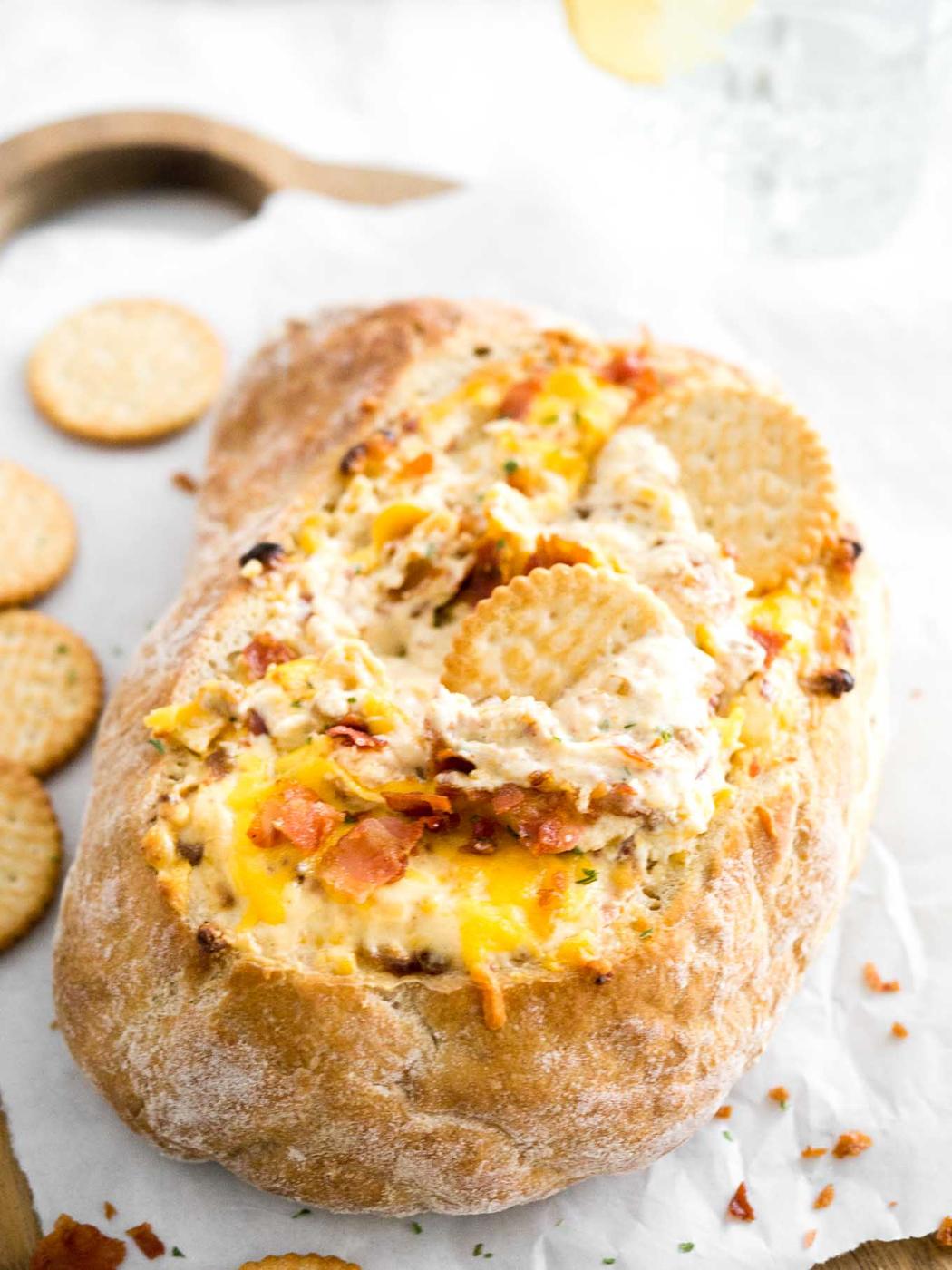 Cheesy bacon onion dip served hot in a round bread bowl with crispy crumbled bacon and parsley on top