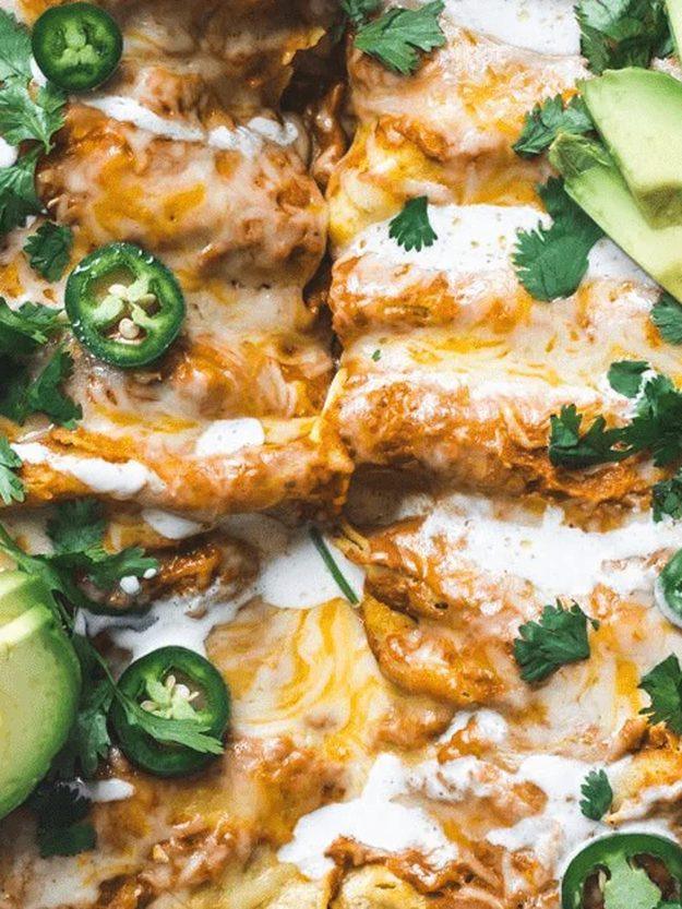 Pan of pumpkin sauce enchiladas topped with melted cheese, jalapeno slices, avocado and fresh cilantro