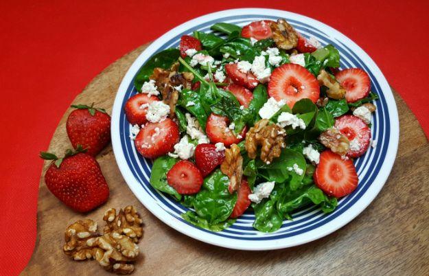 Strawberry feta spinach salad on a blue rimmed plate with sliced berries, walnuts and crumbled feta cheese