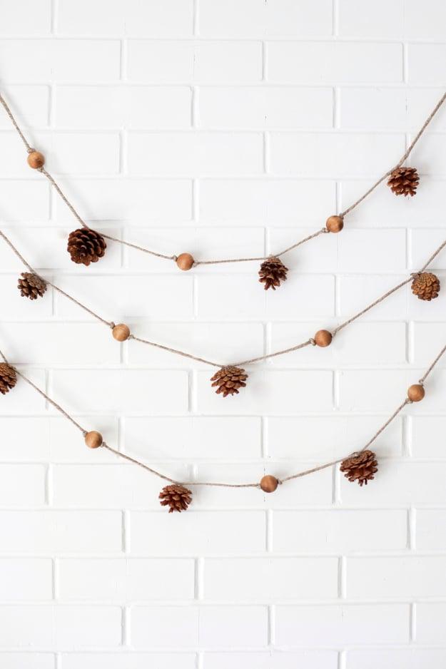Pine cone garland strung on twine with wooden beads knotted in place, draped across a mantel for fall decor