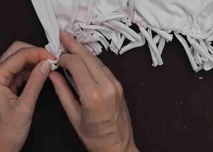 Knotting the fringes to make the bottom of the DIY tote bag