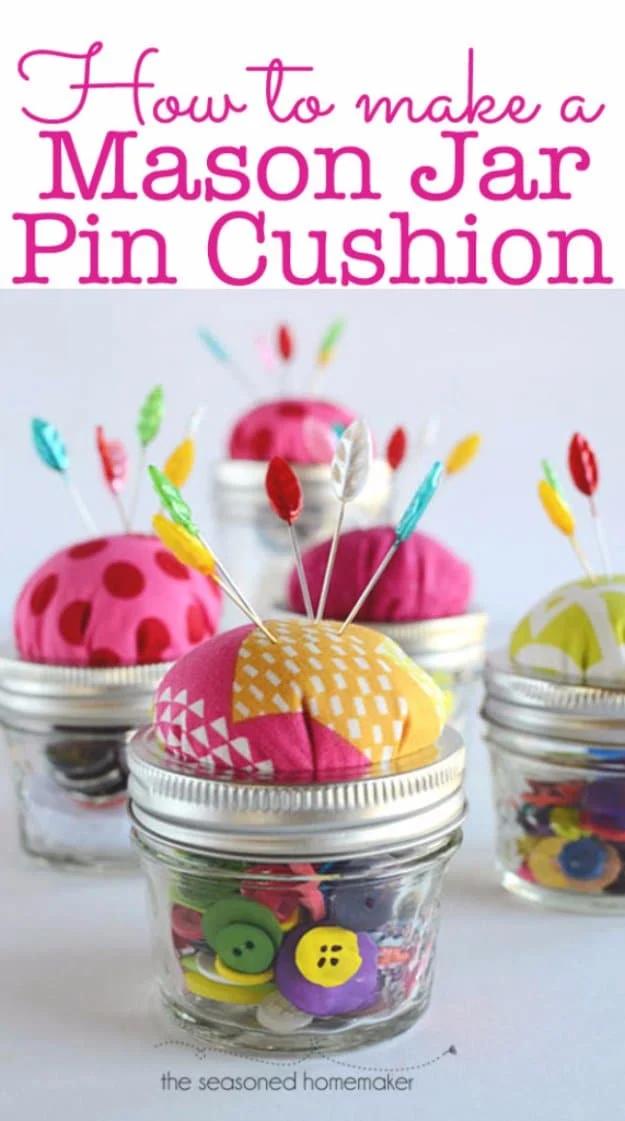 A mason jar topped with a padded blue floral pin cushion dome, its glass body filled with buttons and wooden spools