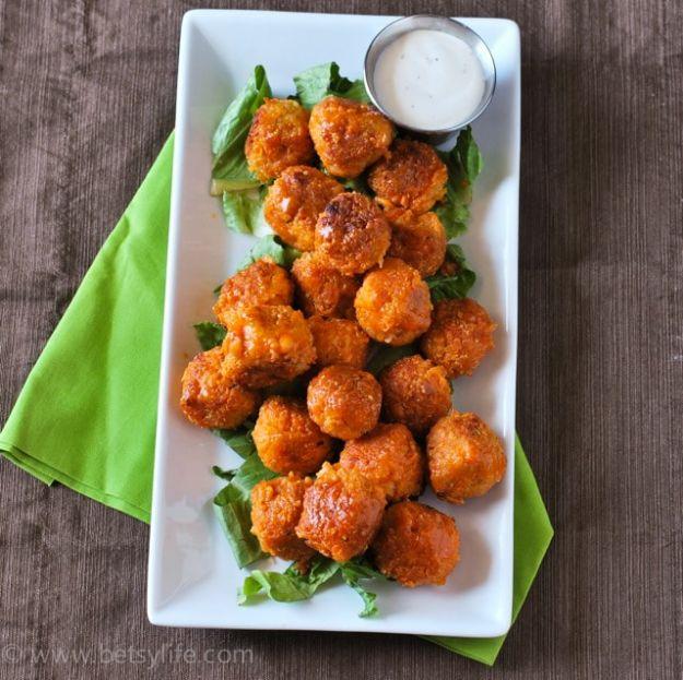 Buffalo quinoa bites on a white platter over greens with a small ramekin of blue cheese dipping sauce