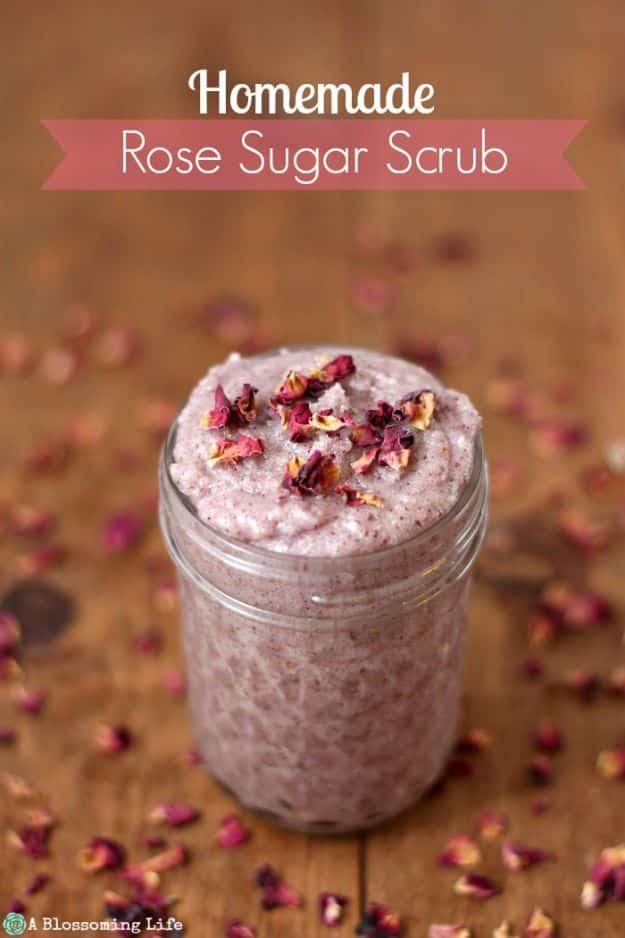 Homemade rose sugar scrub, a mason jar of pale pink scrub topped with dried rosebuds on wood scattered with petals