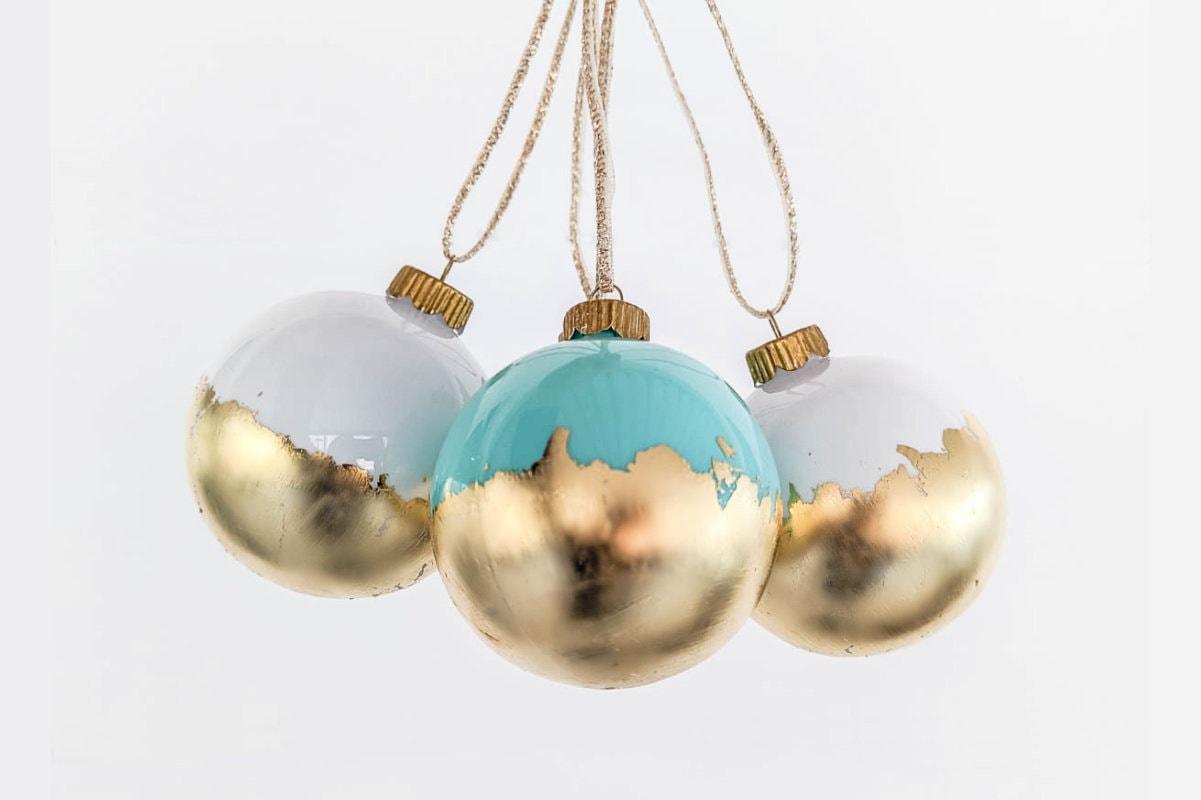 Three glass ball ornaments in white and mint with torn gold leaf across their lower halves, hung on twine