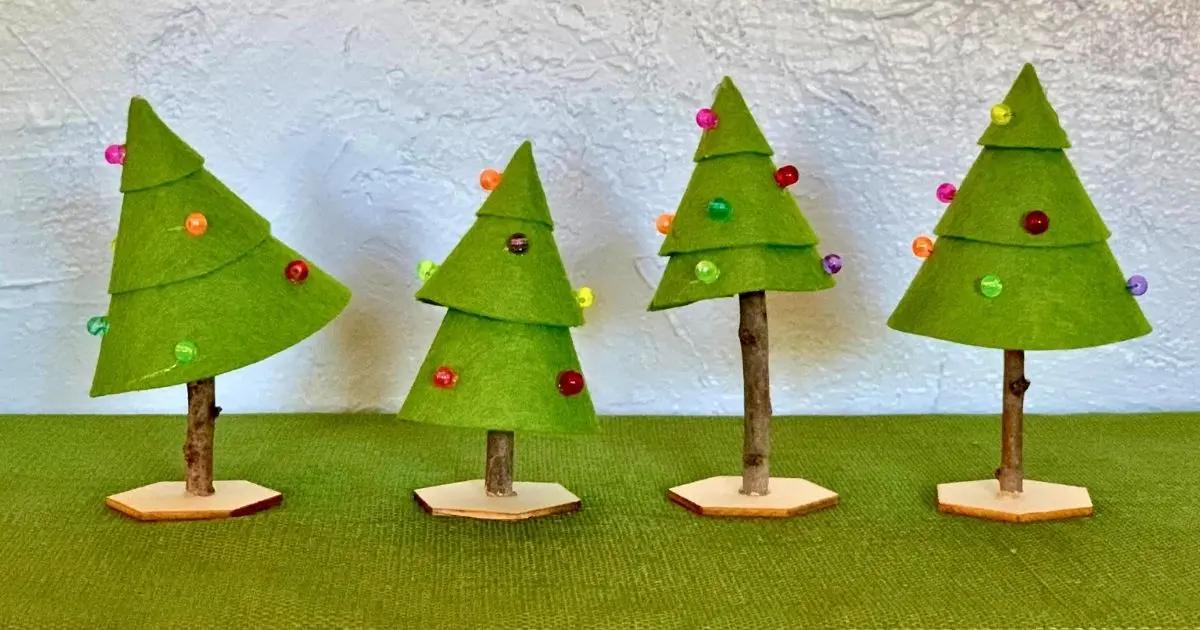 Four green felt cone trees on twig trunks in wooden hexagon bases decorated with colorful pony beads on a green cloth