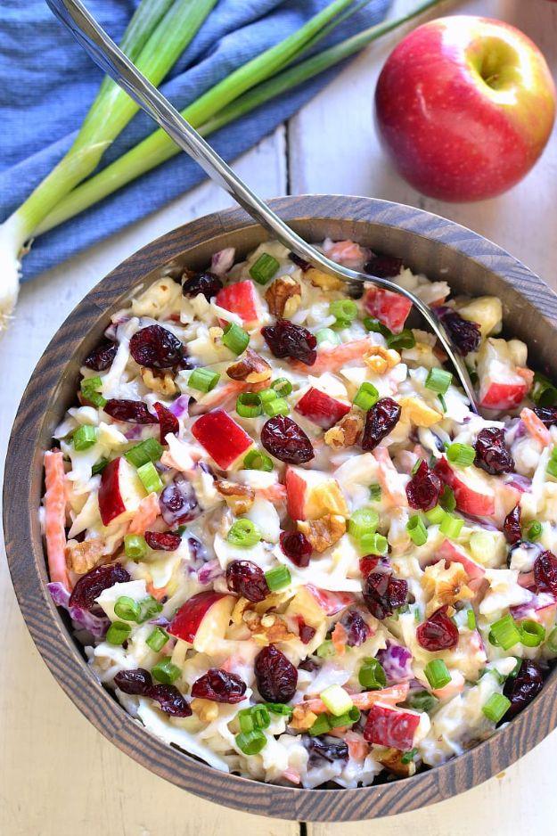 Apple cranberry coleslaw in a wooden bowl with chopped apple, dried cranberries, green onion and a serving spoon