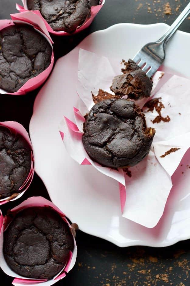 Dark chocolate mocha zucchini muffins in pink paper liners, one broken open with a fork on a white plate