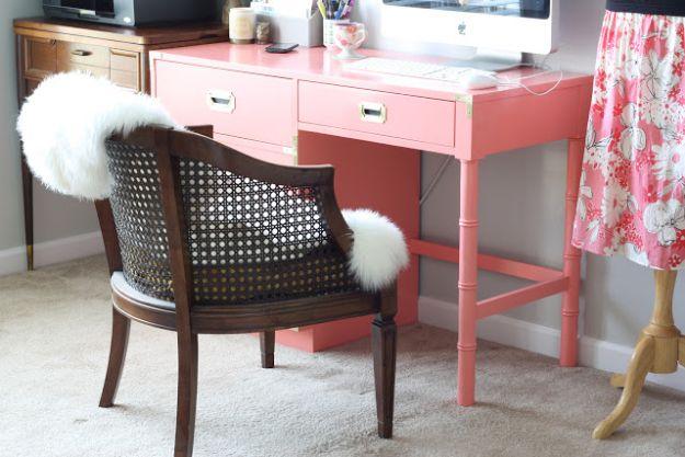 Glossy coral painted vintage campaign desk holding a computer monitor, beside a caned wood chair with a fur throw